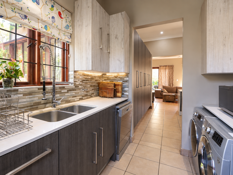 A well-appointed scullery featuring modern cabinetry, a double stainless steel sink, tiled backsplash, and integrated dishwasher, providing efficient additional prep and wash-up space.