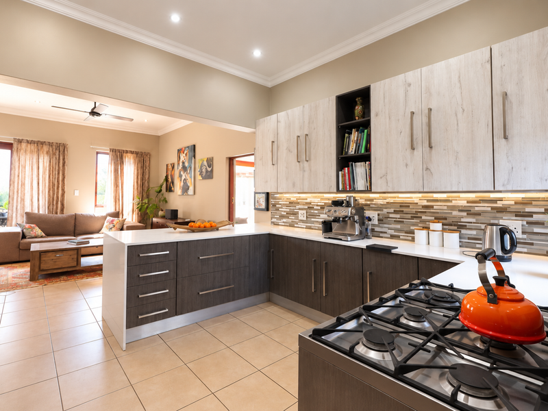 Modern open-plan kitchen featuring two-tone cabinetry, stone countertops, mosaic backsplash, and gas cooktop, seamlessly flowing into the adjacent living area.