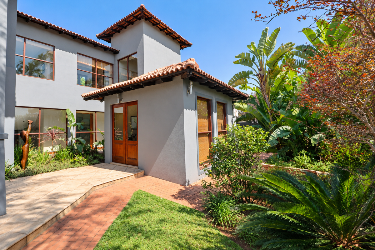 A well-maintained rear exterior view featuring a grey facade, terracotta roof tiles, timber-framed glass doors, and a lush landscaped garden with a paved walkway.