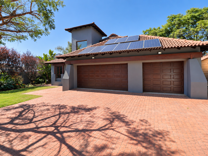 Front view of a well-maintained house featuring a paved driveway, double garage with timber doors, and roof-mounted solar panels.