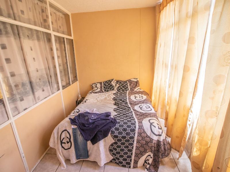 A compact bedroom featuring tiled flooring and a partition wall with glass panels, offering a functional space with potential for cosmetic updates.