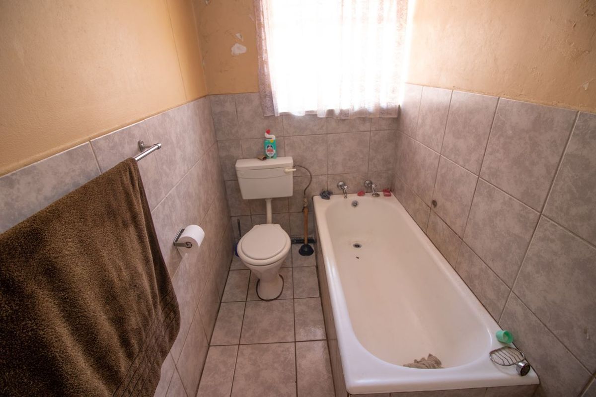 A compact bathroom featuring a standard bathtub, toilet, and neutral wall and floor tiling, currently requiring cosmetic updates to the wall finishes.
