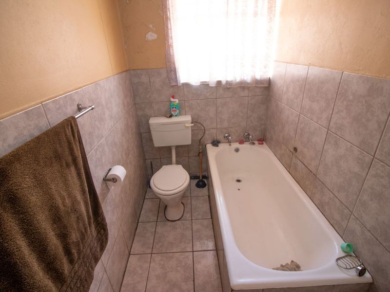 A compact bathroom featuring a standard bathtub, toilet, and neutral wall and floor tiling, currently requiring cosmetic updates to the wall finishes.