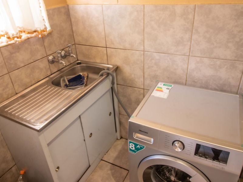 A functional laundry area featuring a stainless steel sink with built-in cabinetry and tiled wall finishes.