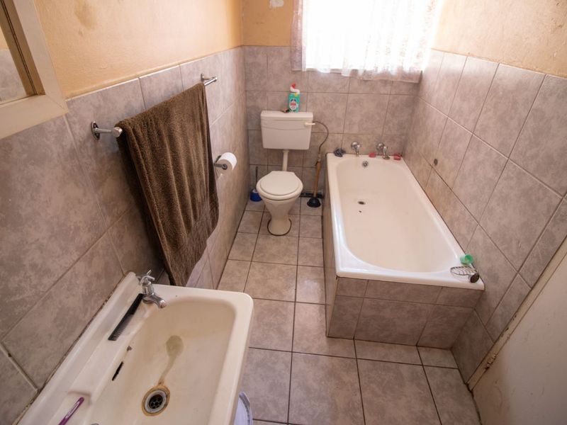 A functional bathroom featuring a bathtub, toilet, and pedestal basin with tiled finishes, requiring cosmetic updates to improve its overall condition.