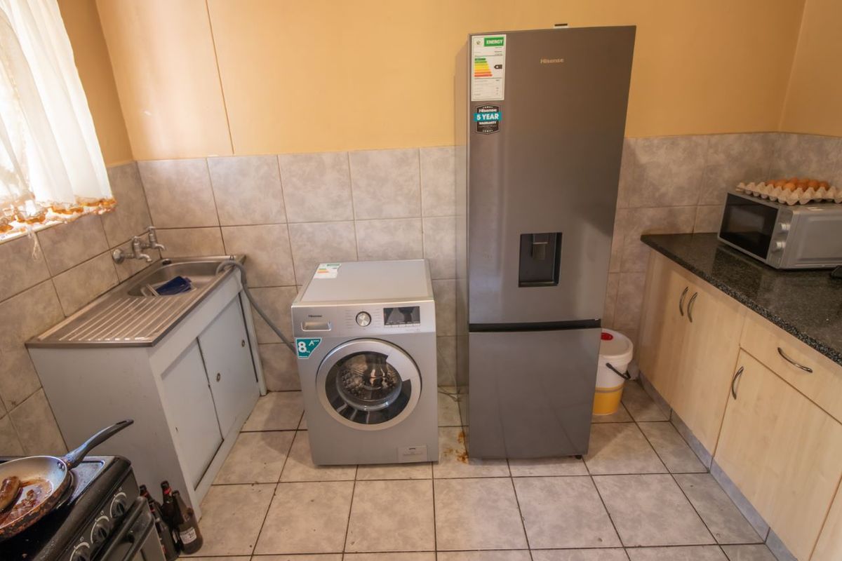 A functional kitchen area featuring tiled splashbacks, laminate cabinetry, granite countertops, and a stainless steel sink with integrated plumbing for laundry appliances.