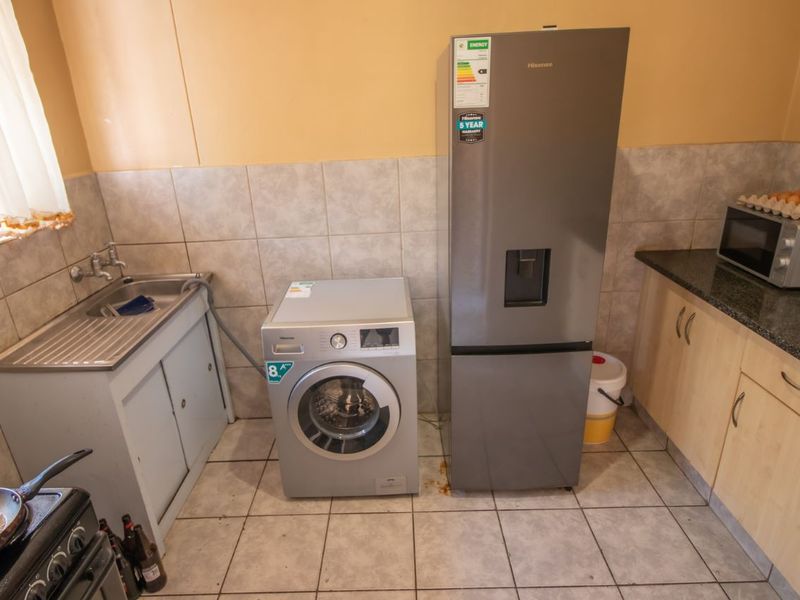 A functional kitchen area featuring tiled splashbacks, laminate cabinetry, granite countertops, and a stainless steel sink with integrated plumbing for laundry appliances.