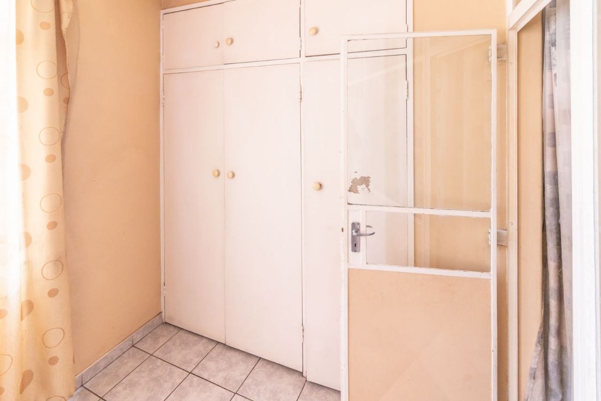 A bedroom featuring built-in cupboards and tiled flooring, currently vacant and in need of cosmetic updates to improve its overall condition.