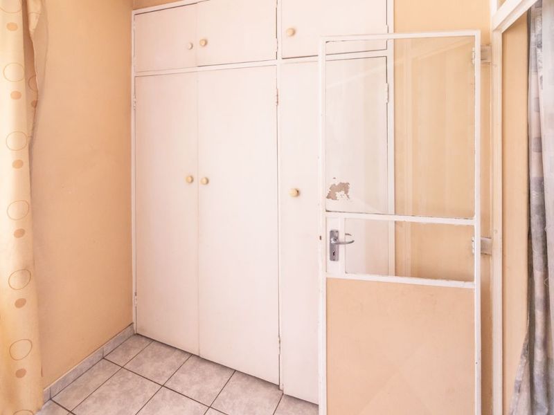 A bedroom featuring built-in cupboards and tiled flooring, currently vacant and in need of cosmetic updates to improve its overall condition.