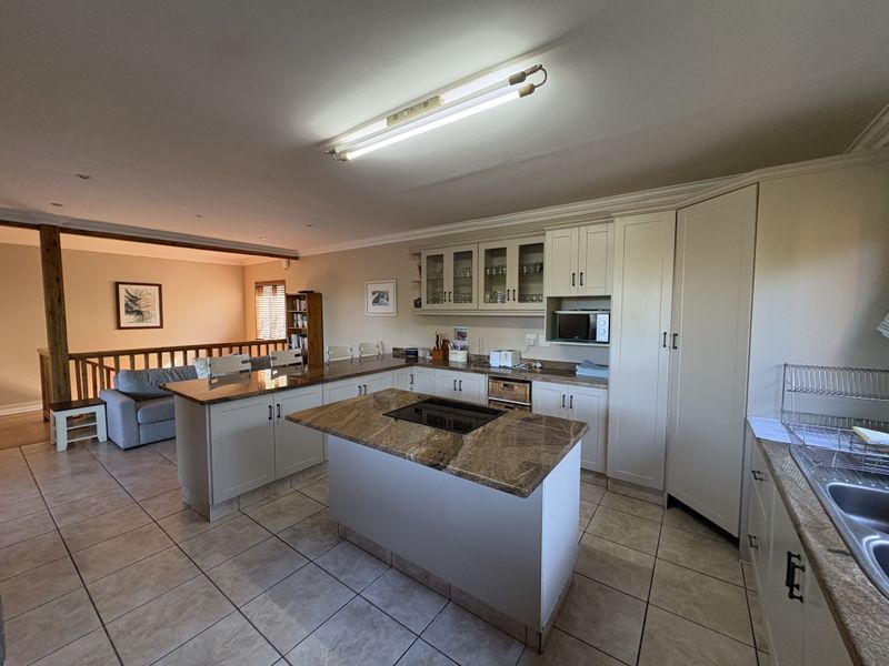 Spacious open-plan kitchen featuring granite countertops, a central island with a built-in hob, and ample cabinetry, seamlessly flowing into the adjacent living area.