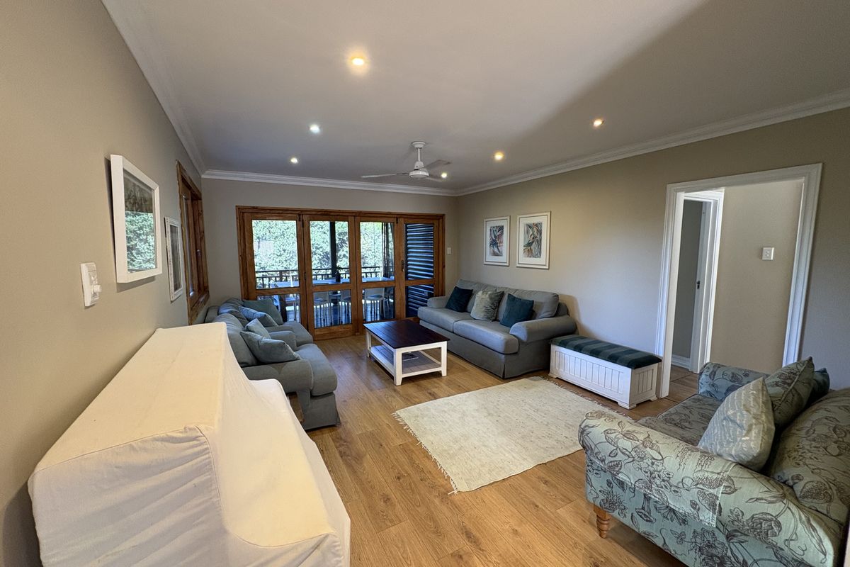 A spacious living room featuring timber flooring, recessed downlights, and wooden framed sliding doors that provide access to an outdoor area.