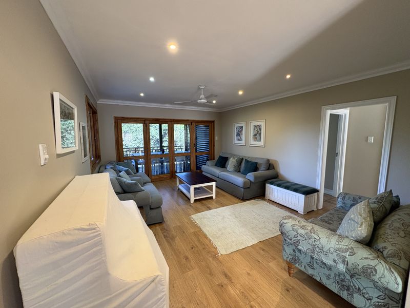 A spacious living room featuring timber flooring, recessed downlights, and wooden framed sliding doors that provide access to an outdoor area.