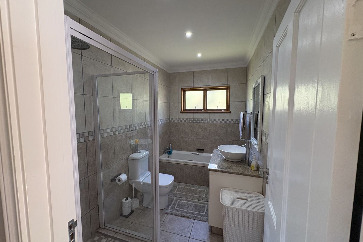 A well-appointed bathroom featuring a glass-enclosed shower, a built-in bathtub, a vanity with a vessel sink, and neutral wall and floor tiling.