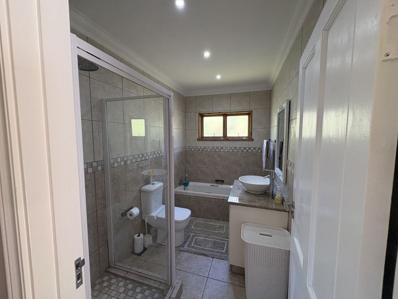 A well-appointed bathroom featuring a glass-enclosed shower, a built-in bathtub, a vanity with a vessel sink, and neutral wall and floor tiling.