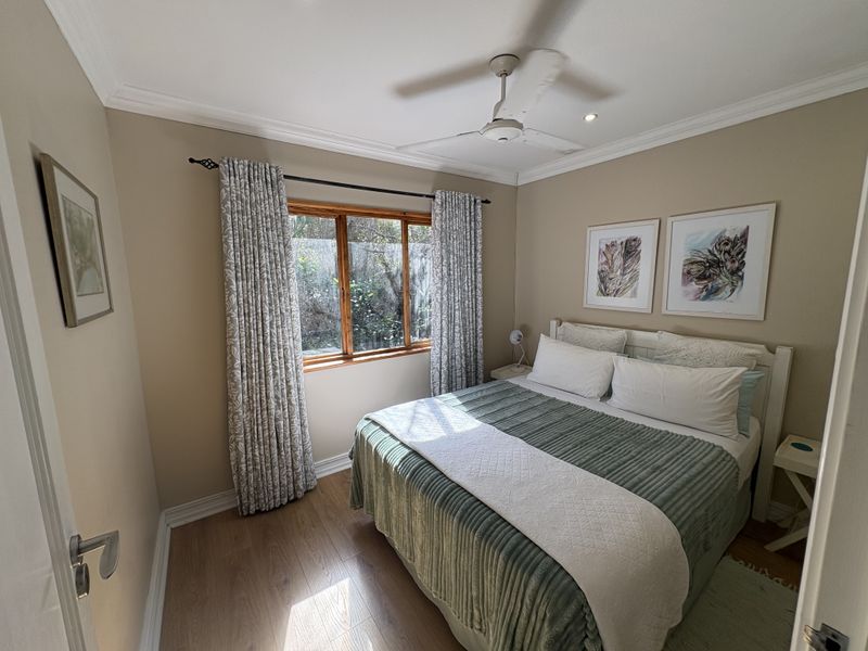 A well-maintained bedroom featuring laminate flooring, a ceiling fan, and a timber-framed window with garden views.