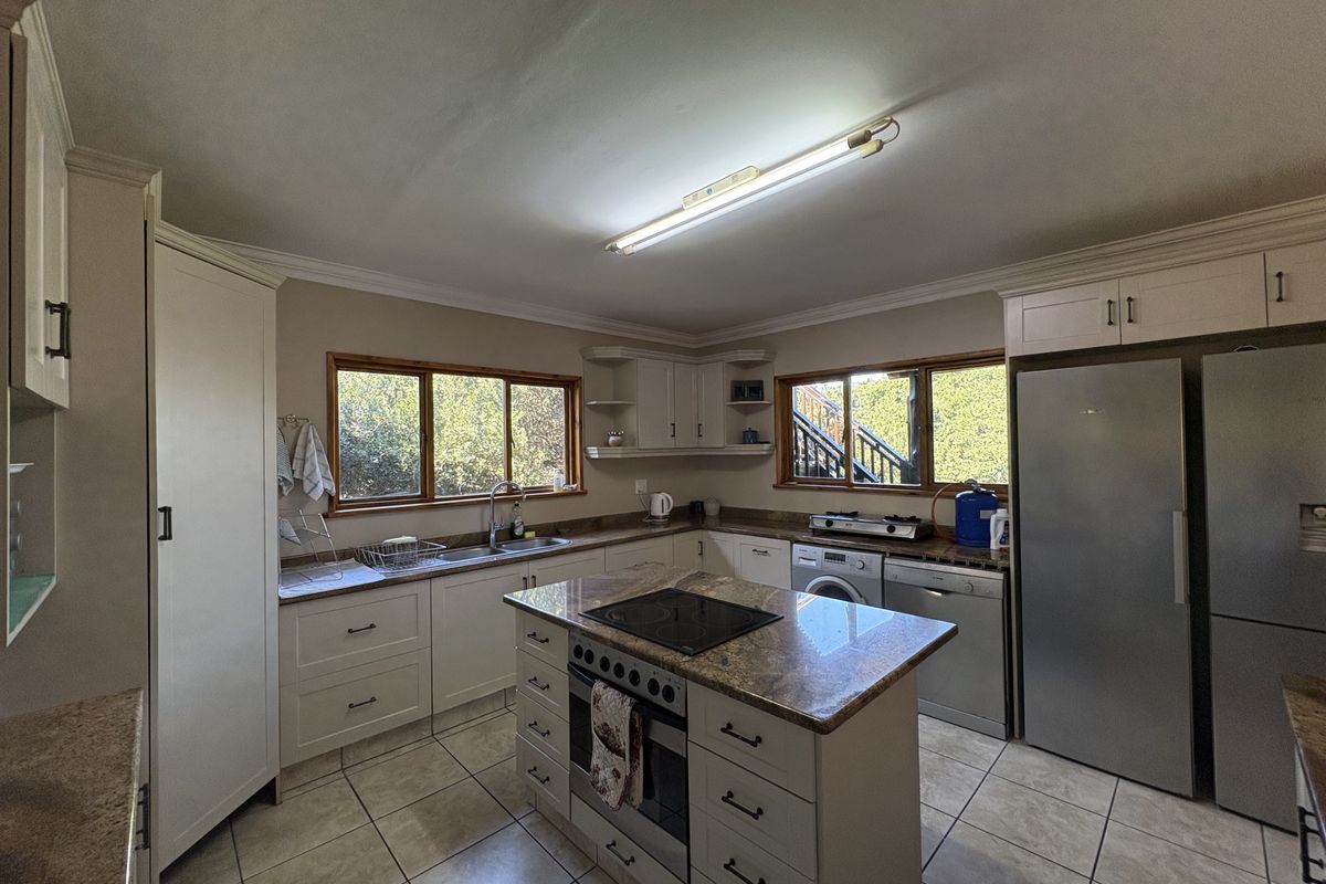 A functional kitchen featuring granite countertops, a central island with a built-in oven and hob, tiled flooring, and ample cabinetry.