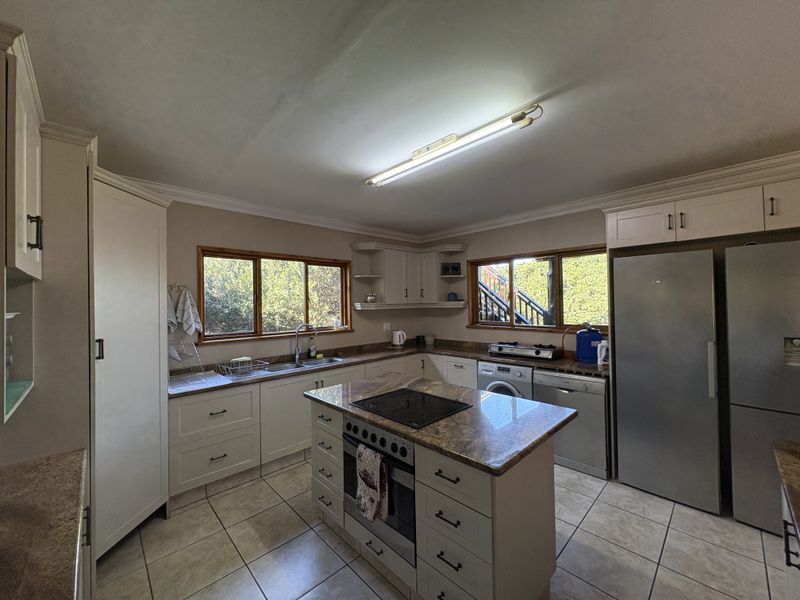 A functional kitchen featuring granite countertops, a central island with a built-in oven and hob, tiled flooring, and ample cabinetry.