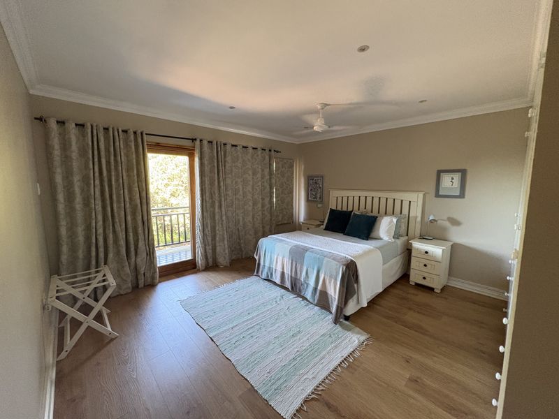 Spacious bedroom featuring laminate flooring, a ceiling fan, and direct access to a private balcony through a glass-paneled door.