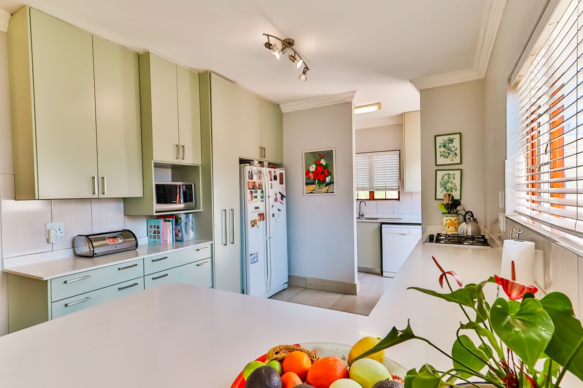 A well-maintained kitchen featuring light green cabinetry, stone countertops, a built-in microwave, and a gas hob, with an adjoining scullery area.