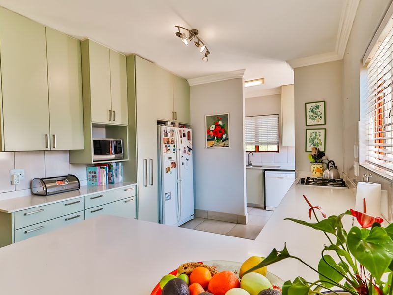A well-maintained kitchen featuring light green cabinetry, stone countertops, a built-in microwave, and a gas hob, with an adjoining scullery area.