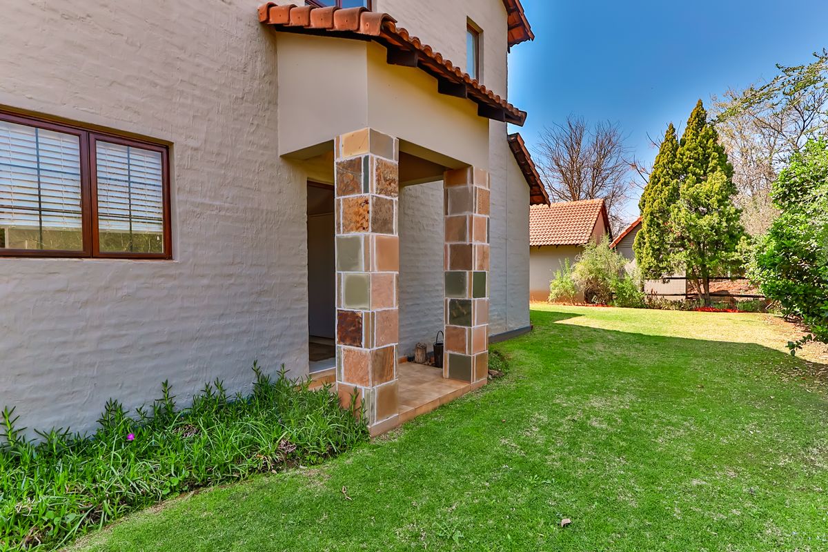 Rear view of the townhouse featuring a covered patio with stone-clad pillars, terracotta roof tiles, and a well-maintained garden lawn.