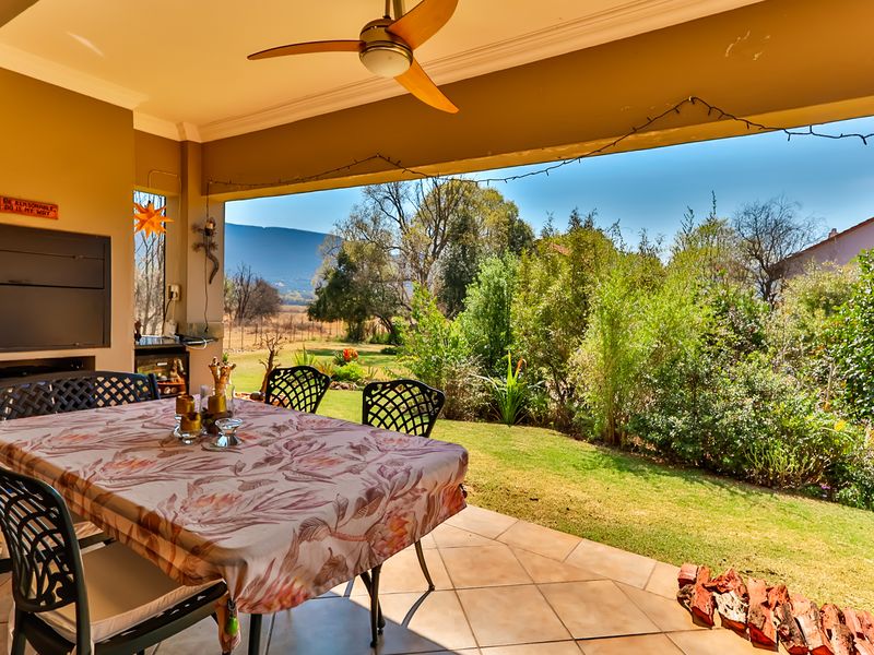 Covered patio featuring a built-in braai, ceiling fan, and tiled flooring, overlooking a landscaped garden with mountain views.