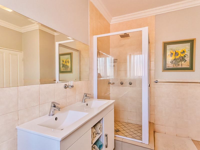 A functional bathroom featuring a double vanity with integrated sinks, a glass-enclosed shower, and neutral wall tiling.