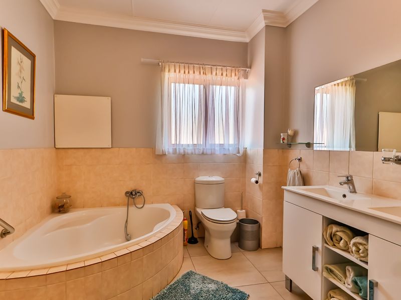 A functional bathroom featuring a corner bathtub, dual basin vanity with storage, and neutral wall tiling.