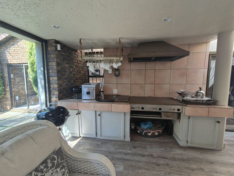Covered outdoor patio area featuring a built-in braai, extractor hood, tiled splashback, and built-in cabinetry, providing a functional space for outdoor cooking and entertaining.