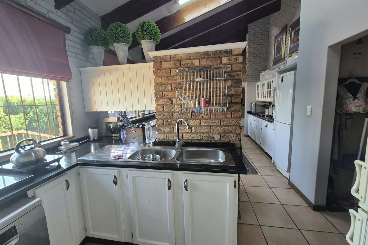 A kitchen featuring exposed timber beams, a brick feature wall, granite countertops, and white cabinetry with a double bowl sink.