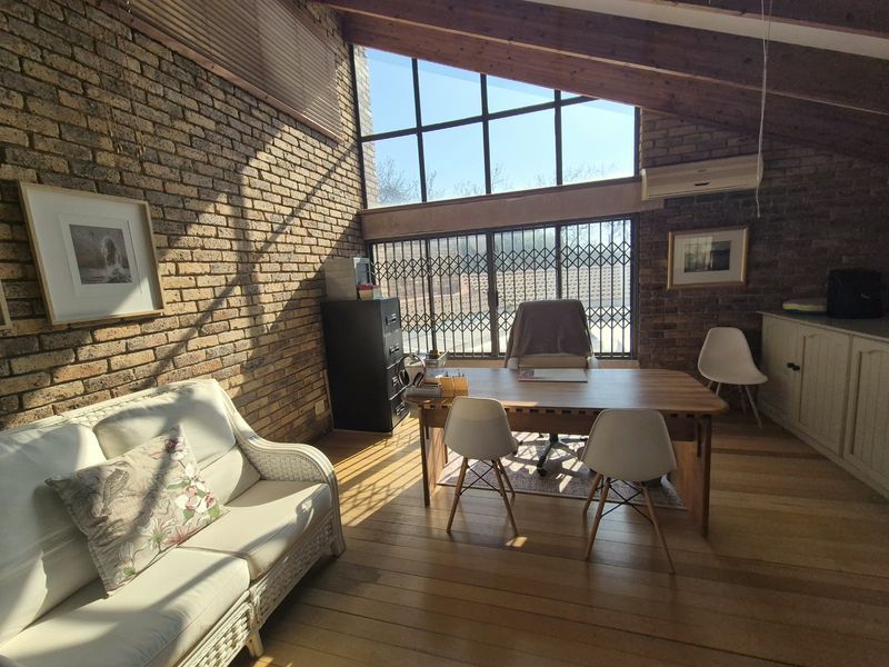 A spacious home office featuring exposed brick walls, vaulted timber ceilings, and large windows that provide ample natural light.