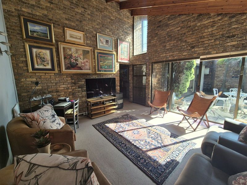 Spacious living room featuring exposed brick walls, high timber-beamed ceilings, and large sliding glass doors providing seamless access to the outdoor patio area.
