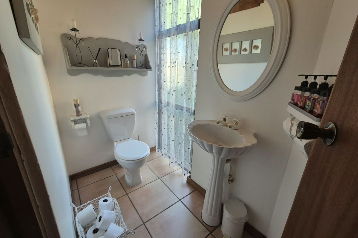 A compact bathroom featuring a pedestal basin, toilet, and tiled flooring, illuminated by a large window with sheer curtains.