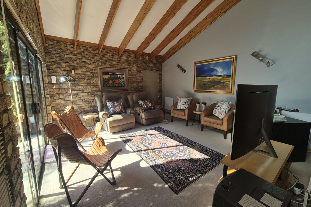 A cozy living room featuring a rustic brick wall, exposed timber ceiling beams, and large sliding glass doors that provide ample natural light.