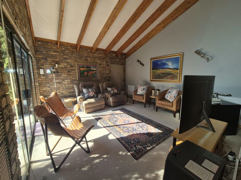 A cozy living room featuring a rustic brick wall, exposed timber ceiling beams, and large sliding glass doors that provide ample natural light.