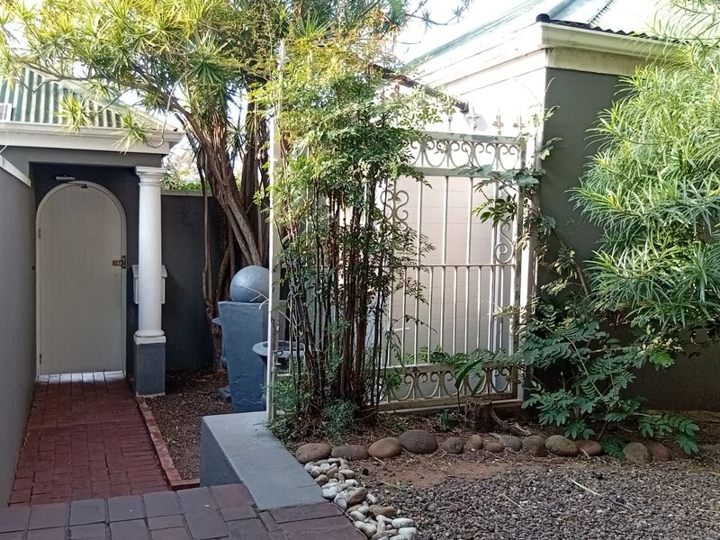 A charming townhouse entrance featuring a brick paved walkway, an arched door with a decorative column, and a wrought iron gate leading to the property.