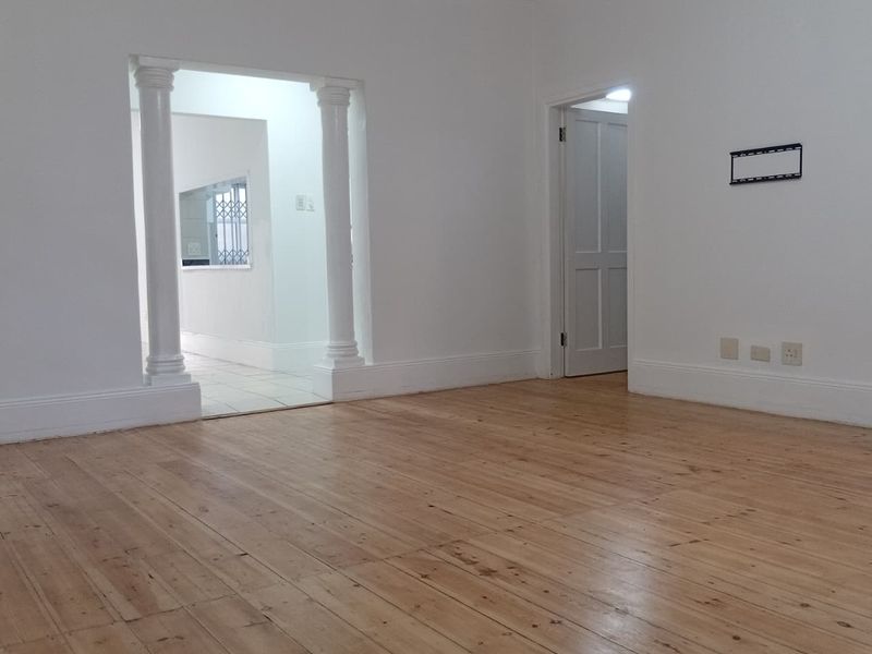An empty living room featuring polished hardwood flooring, decorative columns framing the entryway, and neutral white walls with classic coving.