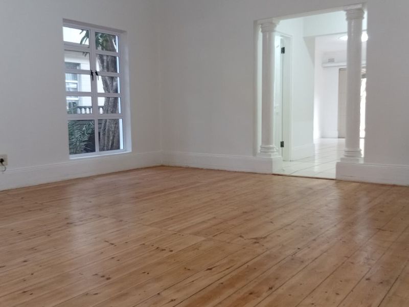 An empty living room featuring polished timber flooring, decorative columns, and coved cornicing, leading into an adjacent tiled hallway.