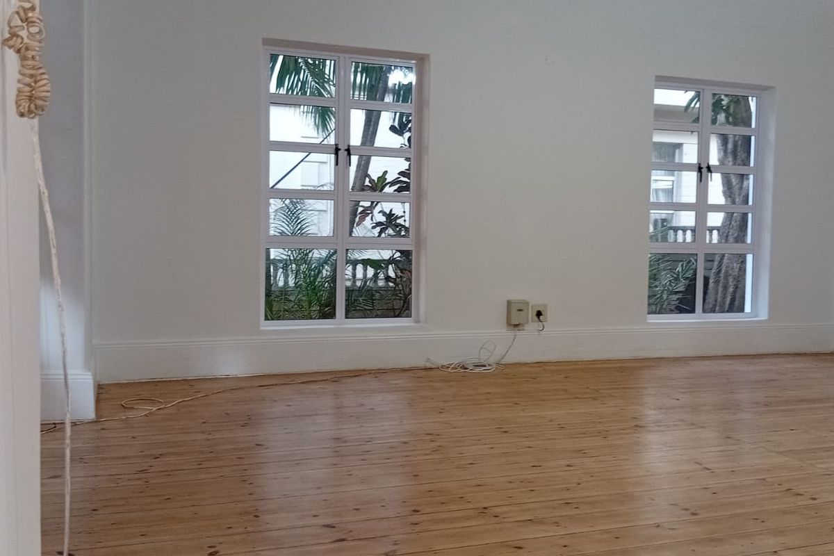 A bright, empty living room featuring polished timber flooring, classic multi-pane windows, and neutral walls, offering a clean canvas for interior design.