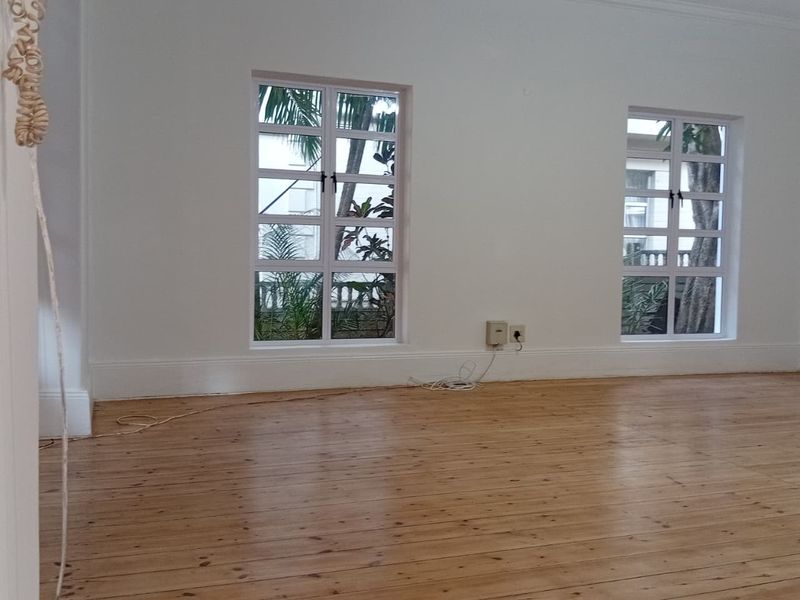 A bright, empty living room featuring polished timber flooring, classic multi-pane windows, and neutral walls, offering a clean canvas for interior design.
