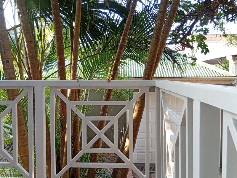 A private balcony featuring a decorative white timber balustrade and tiled flooring, overlooking a lush garden area.