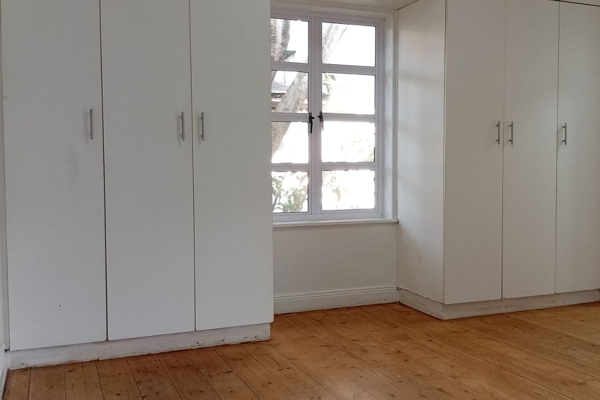 A bright, empty bedroom featuring extensive floor-to-ceiling built-in cupboards and original timber flooring, offering a clean canvas for personalization.