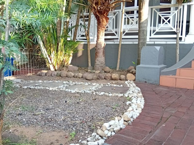 A landscaped garden area featuring brick paving, stone borders, and concrete steps leading to a raised deck with white railings.
