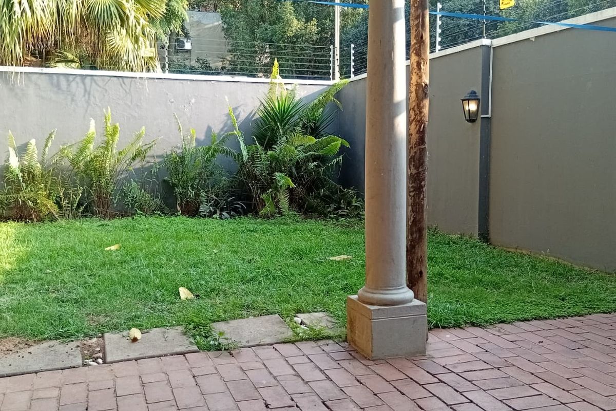 A private rear garden featuring a paved patio area, perimeter wall with electric fencing, and a decorative stone pillar.