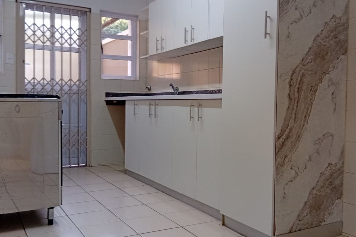 A functional kitchen featuring white cabinetry, tiled flooring, a tiled backsplash, and a security gate leading to the exterior.