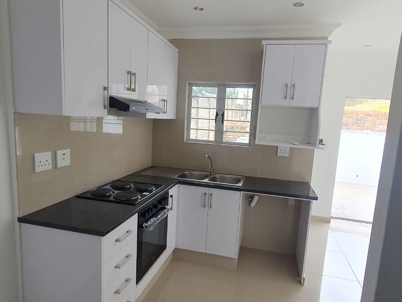 Modern kitchen featuring white cabinetry, dark countertops, built-in electric oven and hob, and a double sink with tiled splashback.
