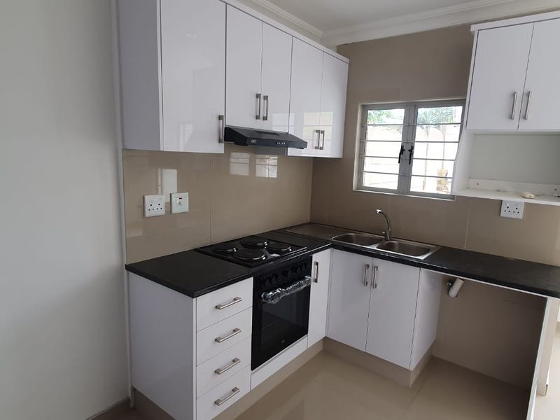 Modern kitchen featuring white high-gloss cabinetry, dark countertops, built-in oven, electric hob, extractor fan, and a double sink with tiled splashback.