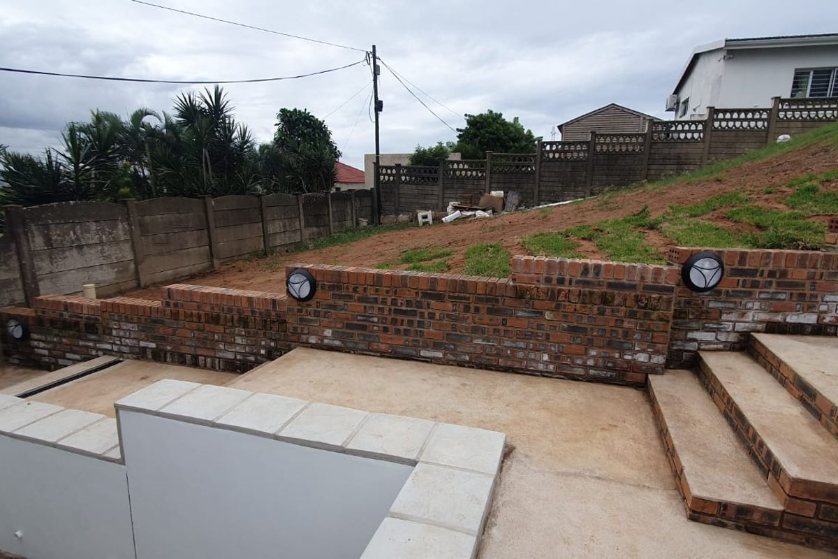 Rear exterior area featuring tiered face brick retaining walls, concrete steps, and a paved patio space with potential for landscaping development.