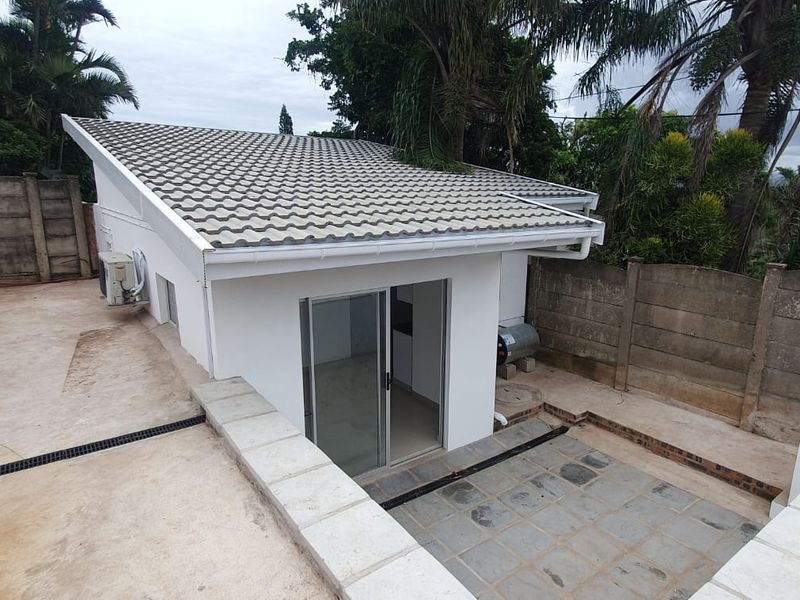 Rear exterior view of the property featuring a tiled roof, sliding glass door access, concrete patio area, and surrounding boundary walls.