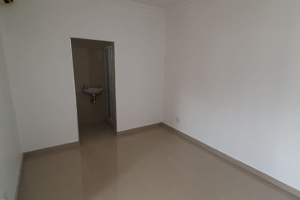 A clean, empty bedroom featuring neutral tiled flooring, white walls, and direct access to an en-suite bathroom.